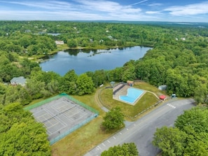 An aerial view of a property with a large lake, a tennis court, and a swimming pool.