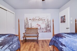 Una camera da letto con due letti, una sedia di legno, un arazzo raffigurante una montagna e una porta decorata con un collage di fotografie.