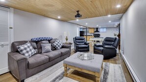 Ein modernes Wohnzimmer mit grauem Sofa, schwarzen Ledersesseln, einem Holztisch und einem Deckenventilator.