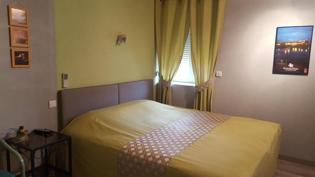 Een hotelkamer met een groot bed, een klein tafeltje en een raam met gordijnen.