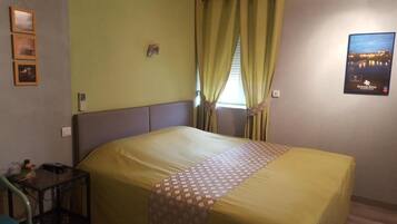 A hotel room with a large bed, a small table, and a window with curtains.