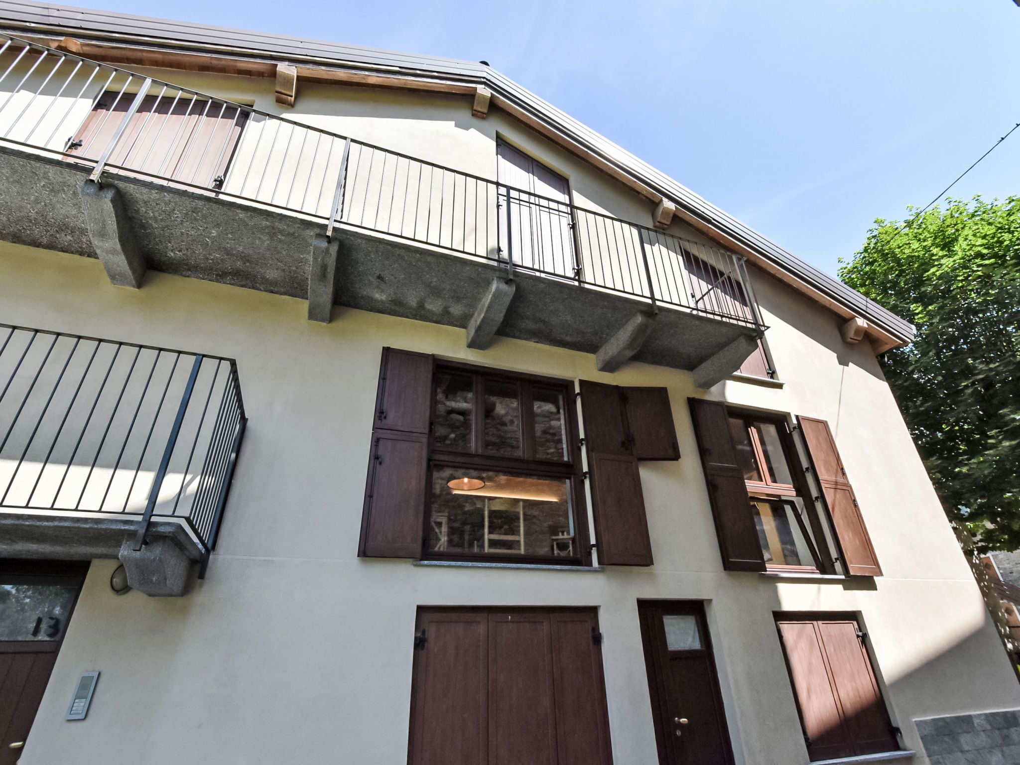 A two-story building with a balcony, large windows with shutters, and a door.