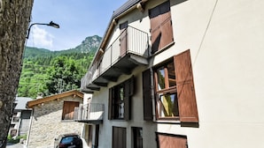 A multi-story building with a balcony, a car parked in front, and a mountainous backdrop. - Ai Tini by Interhome (Campodolcino)