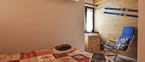 A cozy room with a wooden ceiling, a blue chair with a cushion, a quilted bedspread, and a wooden dresser.