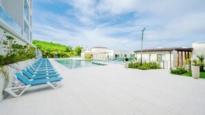 A poolside area with blue lounge chairs, a swimming pool, and a building with a white facade.