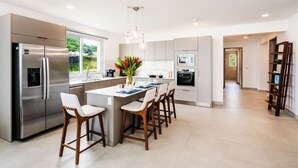 A modern kitchen with a stainless steel refrigerator, a central island with bar stools, and a pendant light.