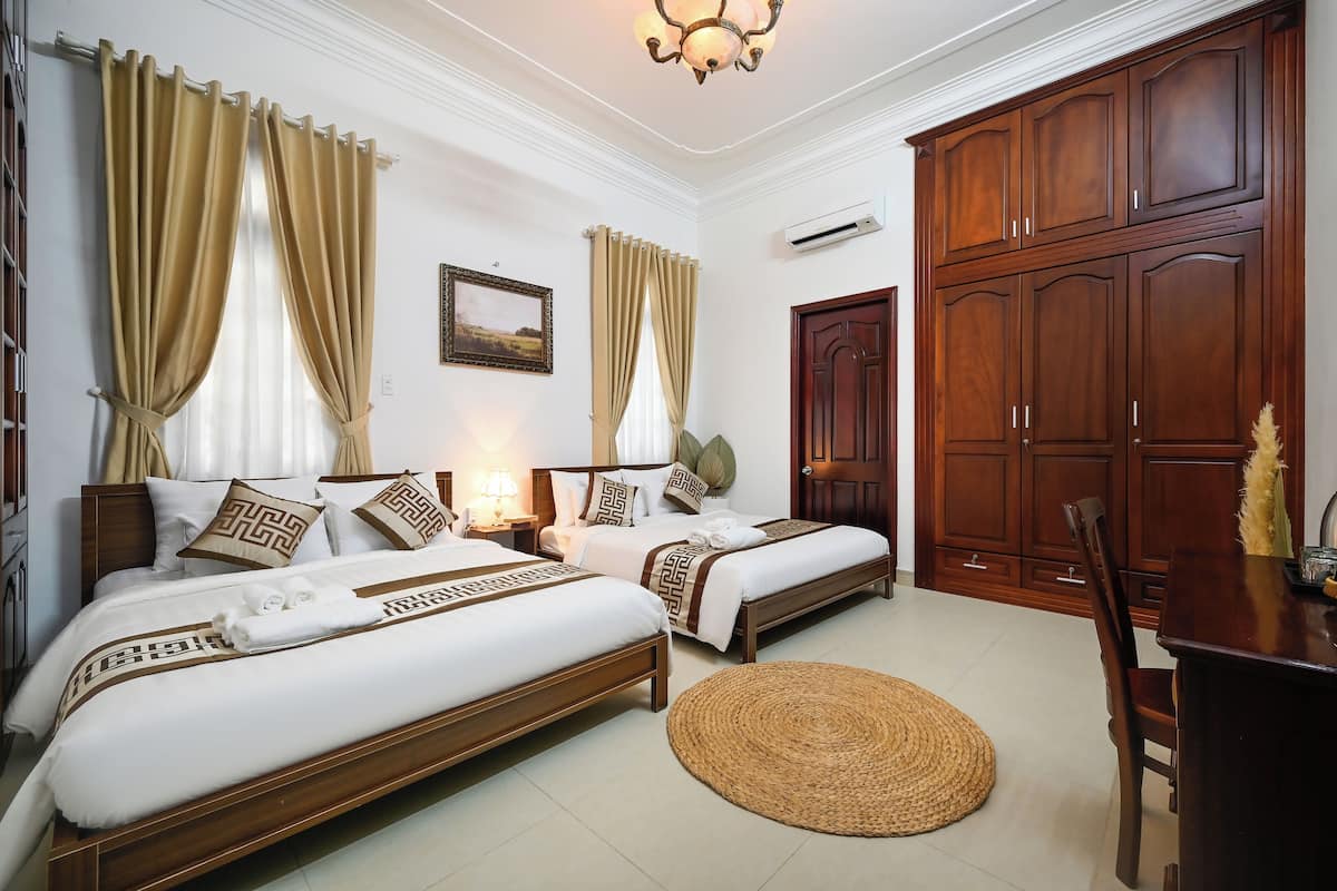 A hotel room with two beds, wooden furniture, a dining table, and a large wardrobe.