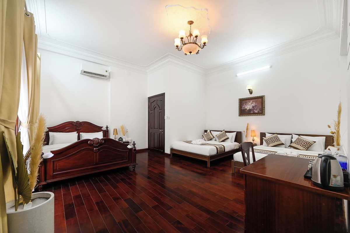 A hotel room with a wooden bed, a sofa, a desk, and a chandelier.