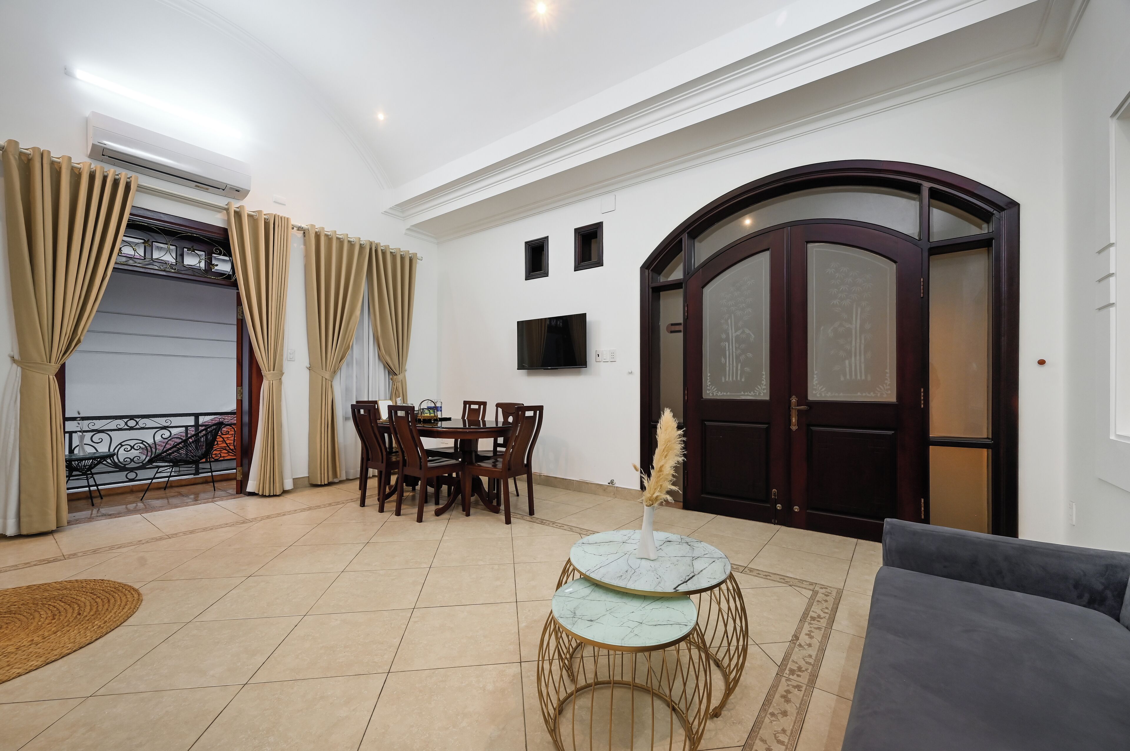 A living room with a dining area, a TV mounted on the wall, and a large wooden door with glass panels.