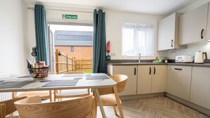 Una cocina moderna con armarios de madera, una mesa de comedor con sillas, un extintor y vistas a un edificio de ladrillo.