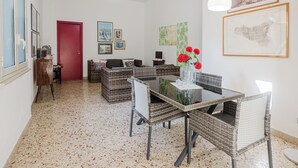 Un comedor con muebles de mimbre, una mesa de vidrio y un jarrón con flores rojas.