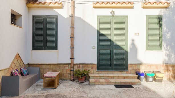 Un edificio con contraventanas verdes, un acceso con azulejos y un pequeño banco con cojines coloridos.