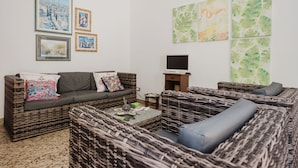 Una sala de estar con muebles de mimbre, televisor y decoración en las paredes.