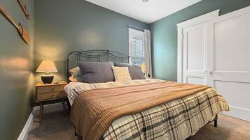A bedroom with a bed, a nightstand, a lamp, a window with blinds, and a door.