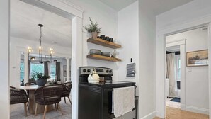 A modern kitchen with a black stove, wooden shelves, and a dining area with wicker chairs.
