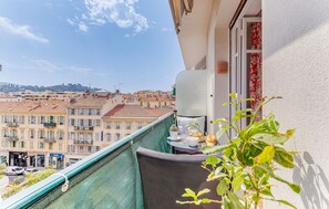 A balcony with a view of a cityscape, a table with a plant, and a window with a curtain.
