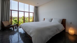 A large bed with a wooden headboard, a bedside table, and a lamp. There is a window with curtains, and a chair is visible in the corner. - Scarlet Pavilion Homestay (Hue)