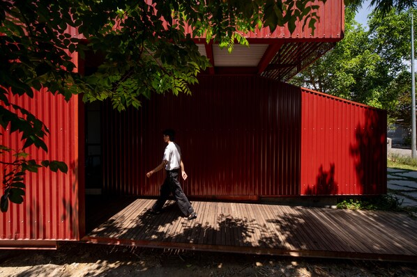 A person walking on a wooden deck in front of a red building with a corrugated metal exterior. - Scarlet Pavilion Homestay (Hue)