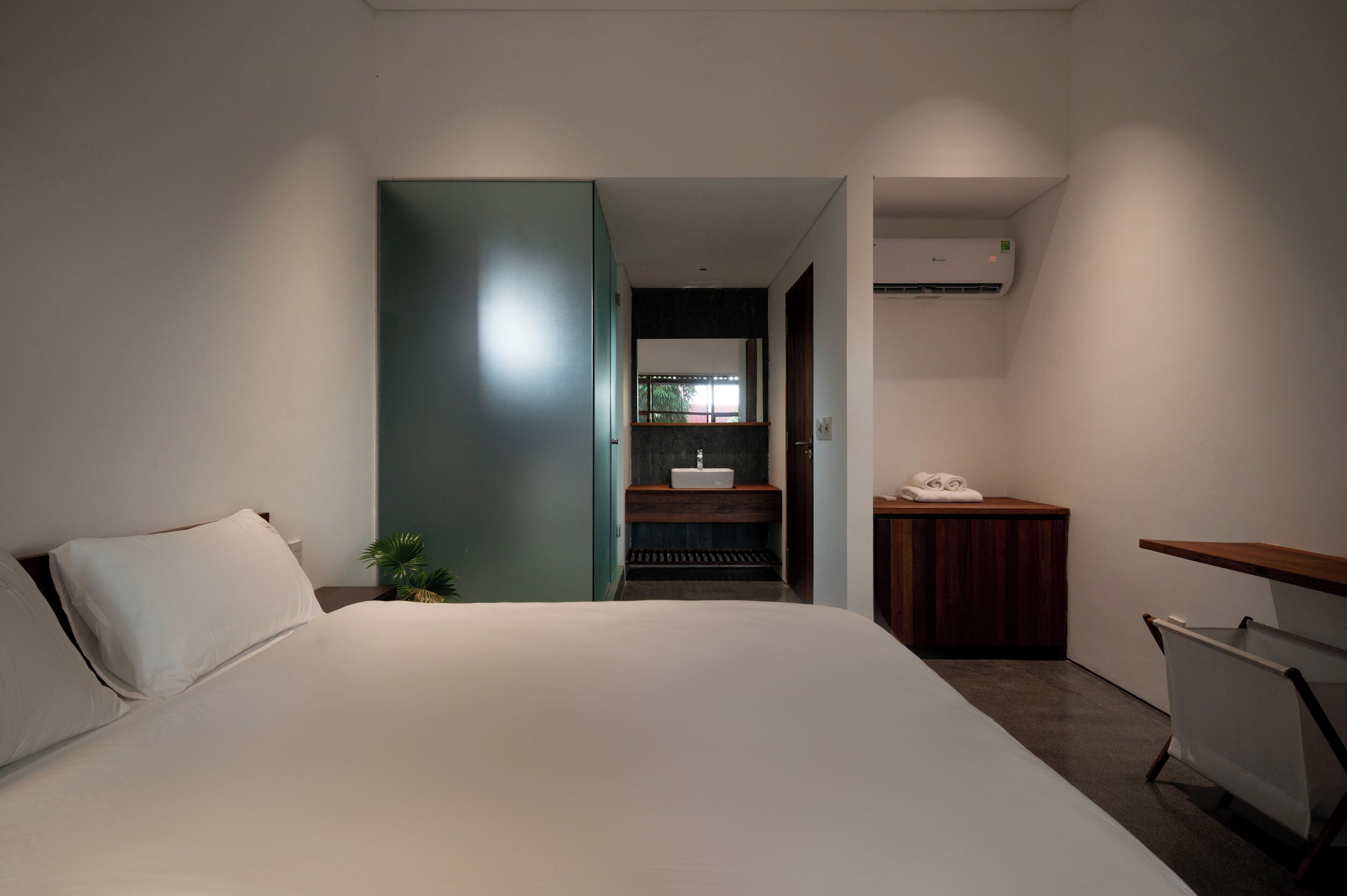 A modern hotel room with a large bed, a small bathroom with a sink, and a wooden side table.