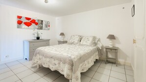 Un dormitorio con cama, mesitas de noche, cómoda, un cuadro y una lámpara.