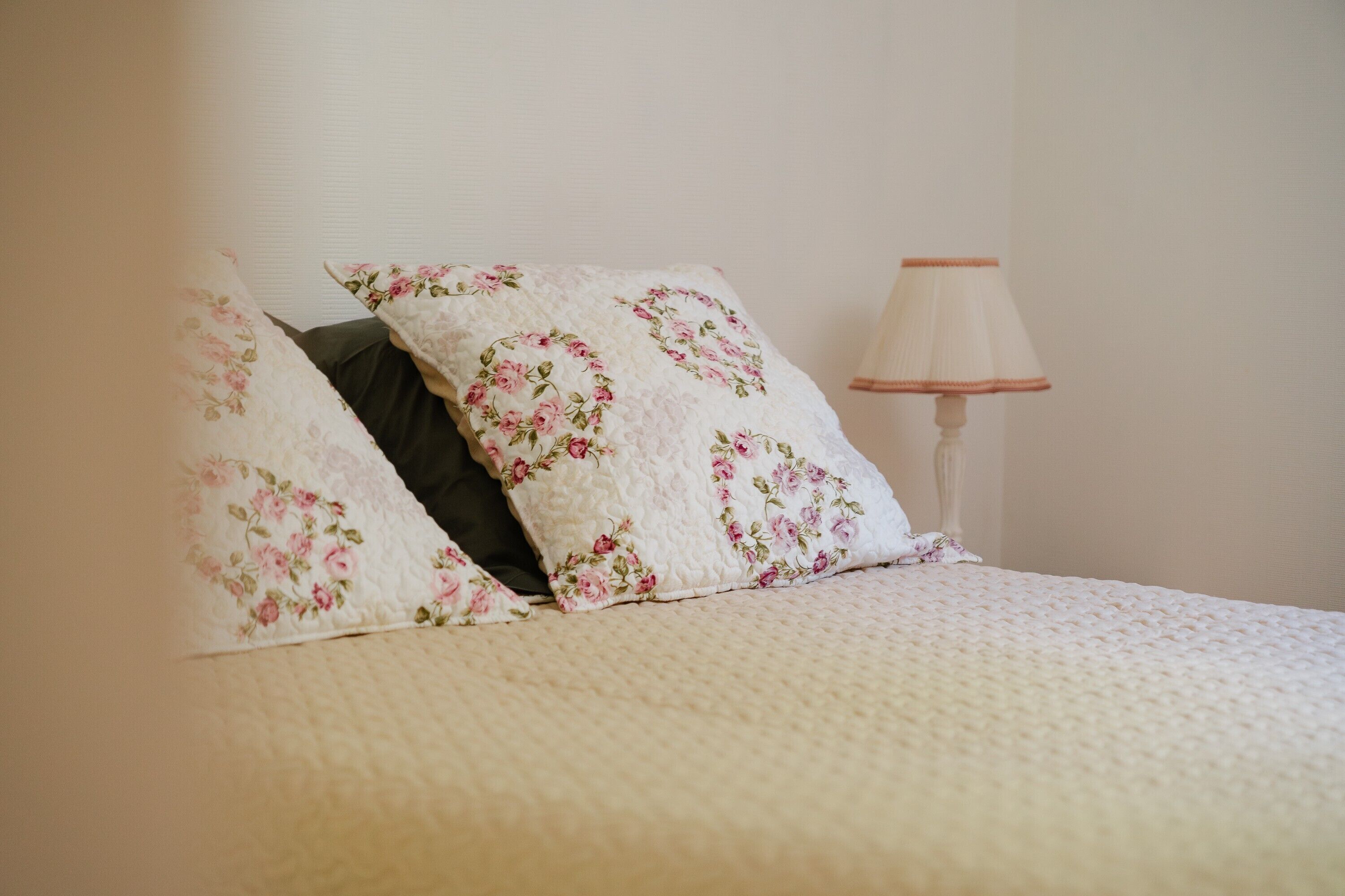 A bed with floral-patterned pillows and a bedside lamp.
