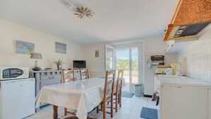 Una cocina con una mesa de comedor, sillas, microondas, refrigerador y ventana con vistas.