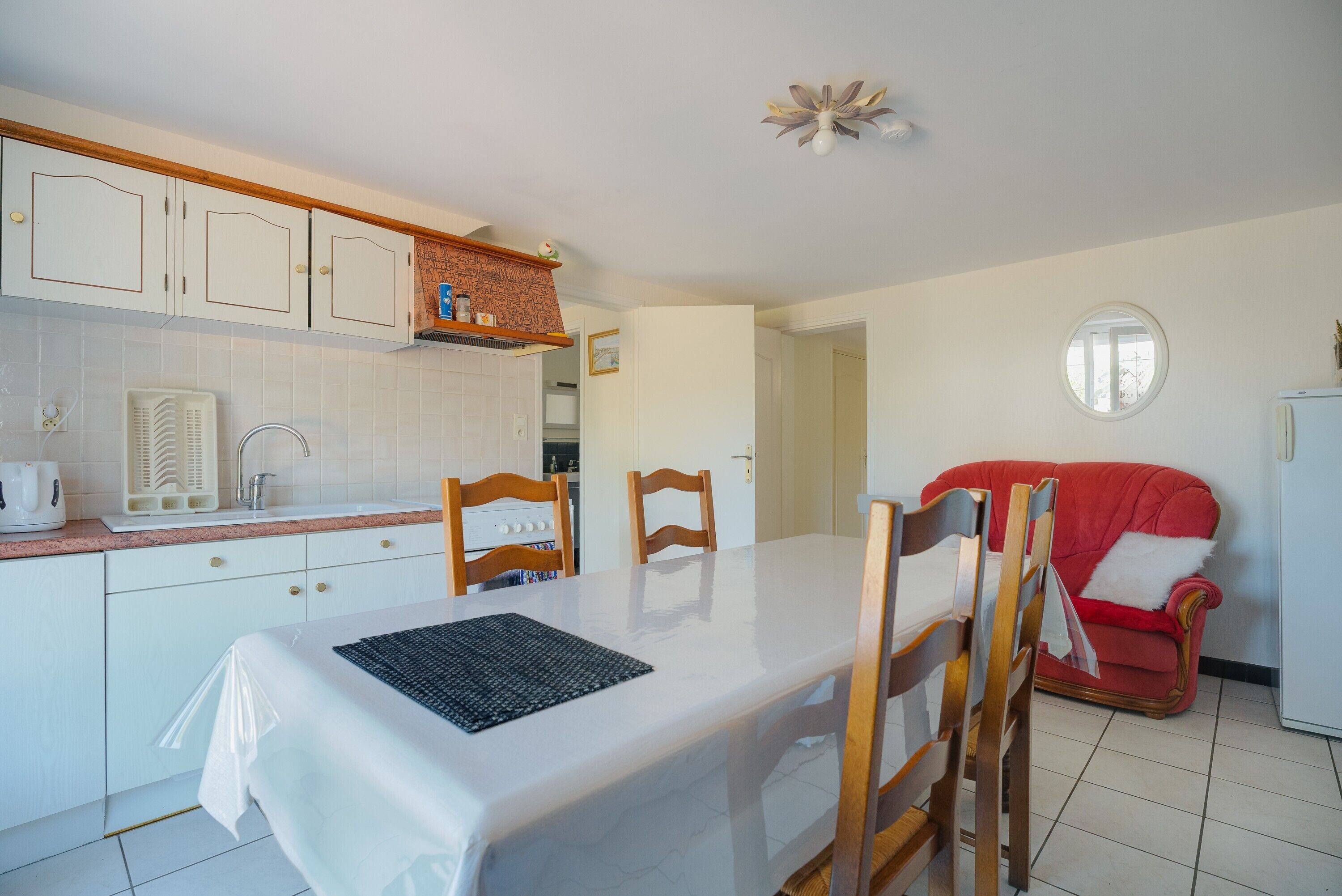 Eine Küche mit weißen Schränken, einem Esstisch mit Stühlen, einem roten Sofa und einem kleinen Fenster.