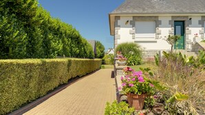 Una casa con entrada pavimentada, puerta verde y jardín cuidado con diversas plantas y flores.