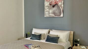 Une chambre à coucher avec un lit, des oreillers, un magazine, un tableau et une table de chevet sur laquelle se trouve une plante.