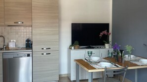 Een moderne keuken met een vaatwasser, een flatscreen televisie en een eethoek met een tafel, stoelen en decoratieve accessoires.