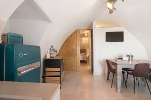 Une cuisine de taille réduite avec un réfrigérateur de couleur turquoise, des placards en bois, une table à manger avec des chaises et un téléviseur fixé au mur.