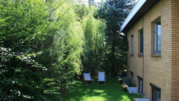 A backyard with a lawn, two striped chairs, and a brick building with windows.