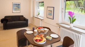 A dining area with a table set for breakfast, including fruits and pastries, and a couch in the background.