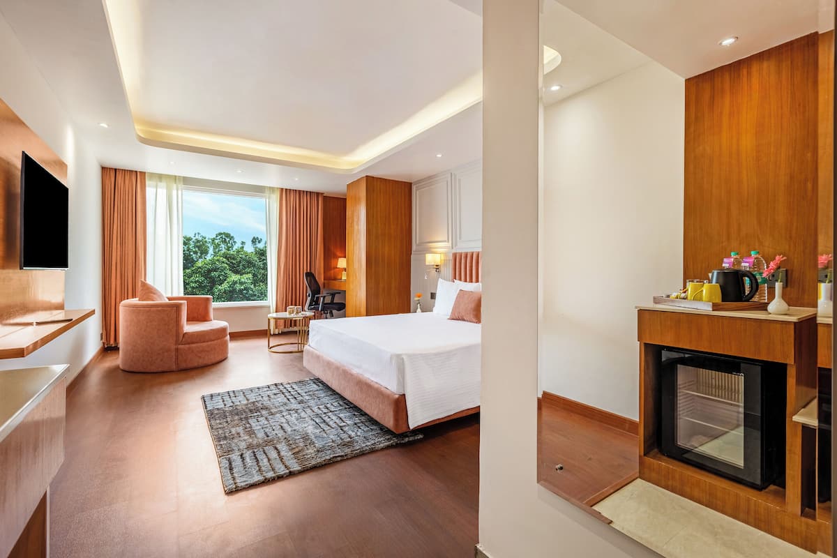 Une chambre d’hôtel moderne équipée d’un lit, d’un bureau, d’une chaise, d’une cheminée et d’une grande fenêtre donnant sur la forêt.