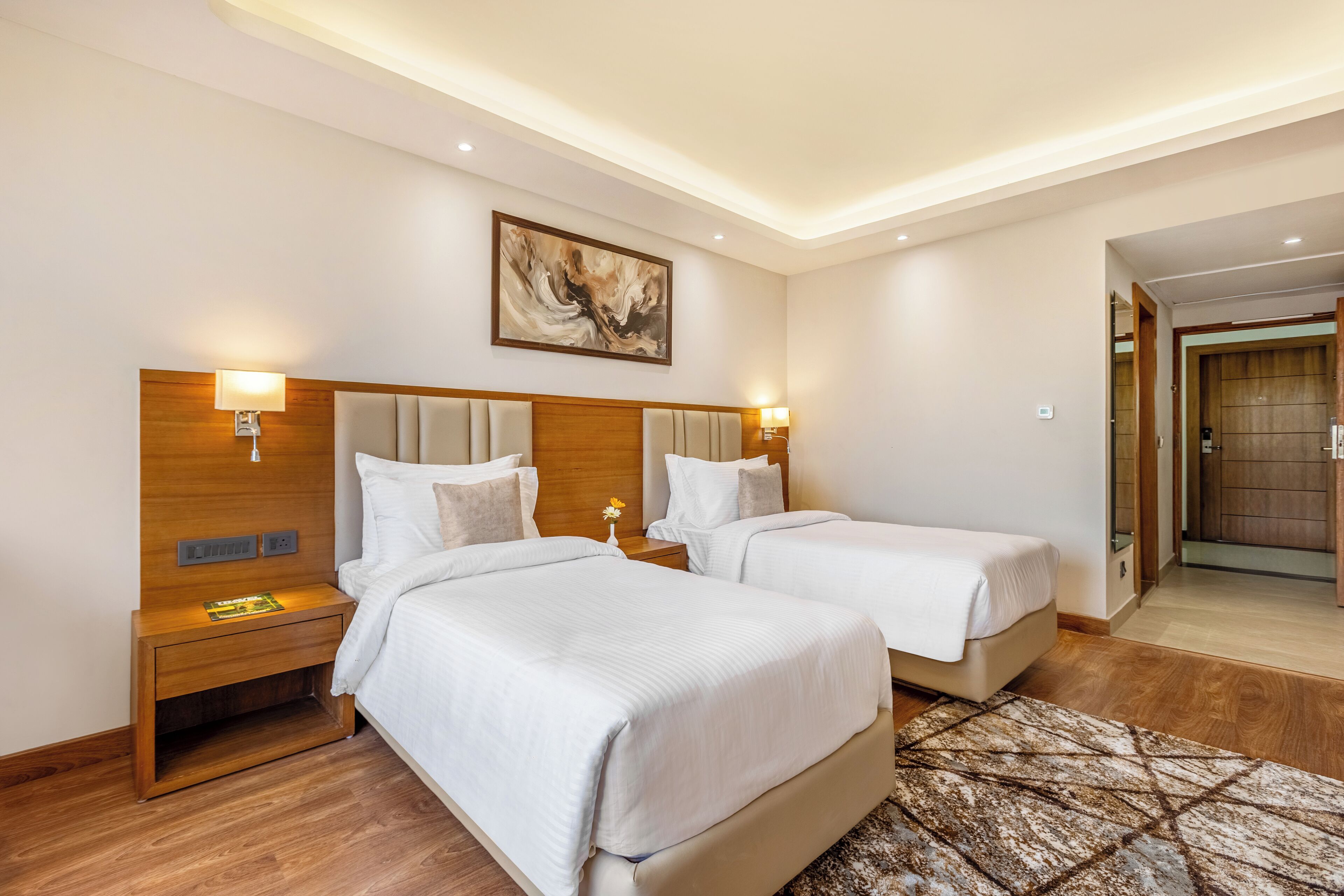 Una habitación de hotel con dos camas, cabeceros de madera, lámparas de noche y un cuadro en la pared.
