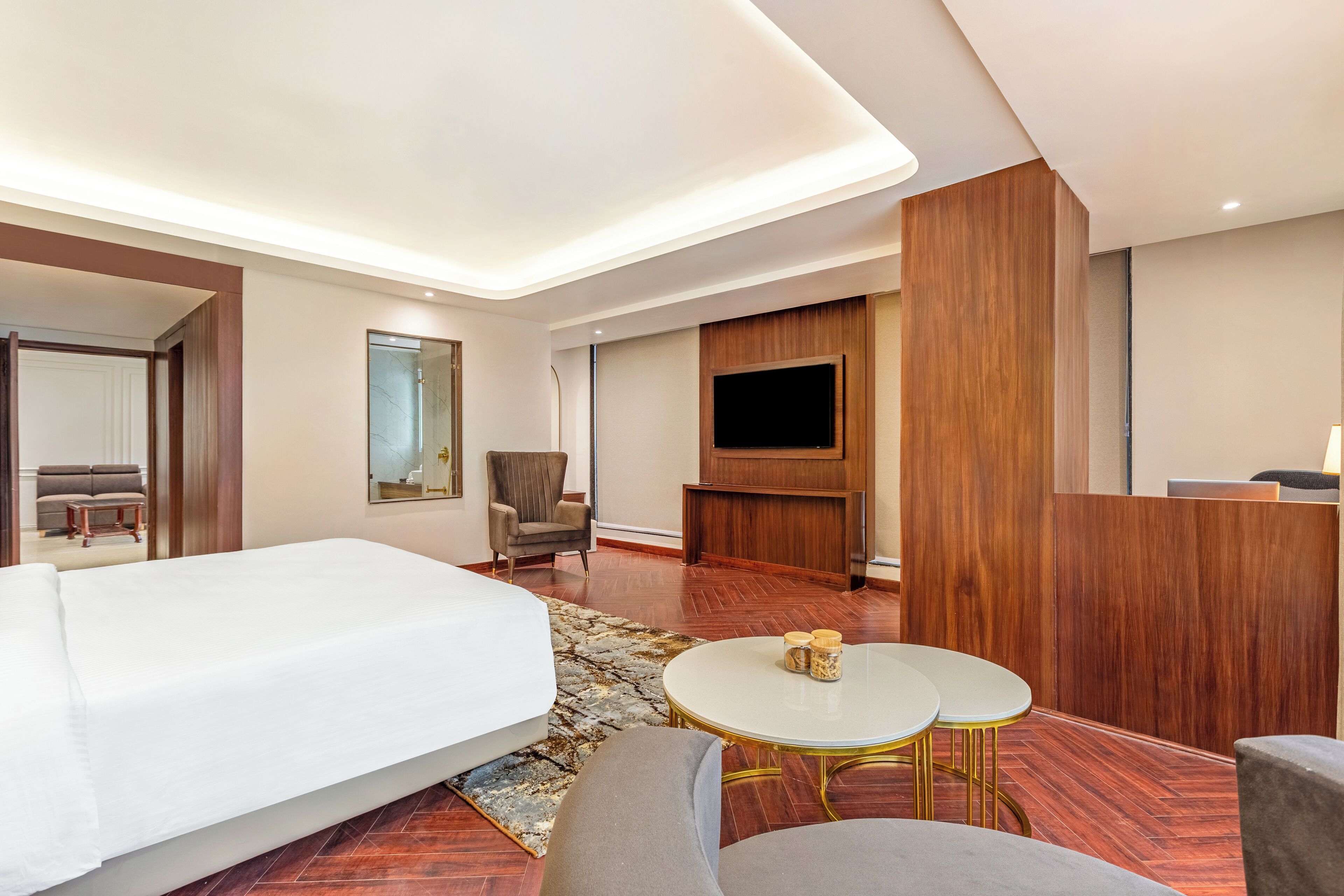 A hotel room with a large bed, a TV, a seating area with two chairs and a small table, and a wooden panel wall.