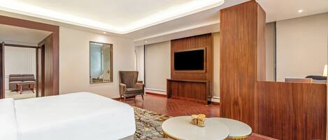 A hotel room with a large bed, a TV, a seating area with two chairs and a small table, and a wooden panel wall.