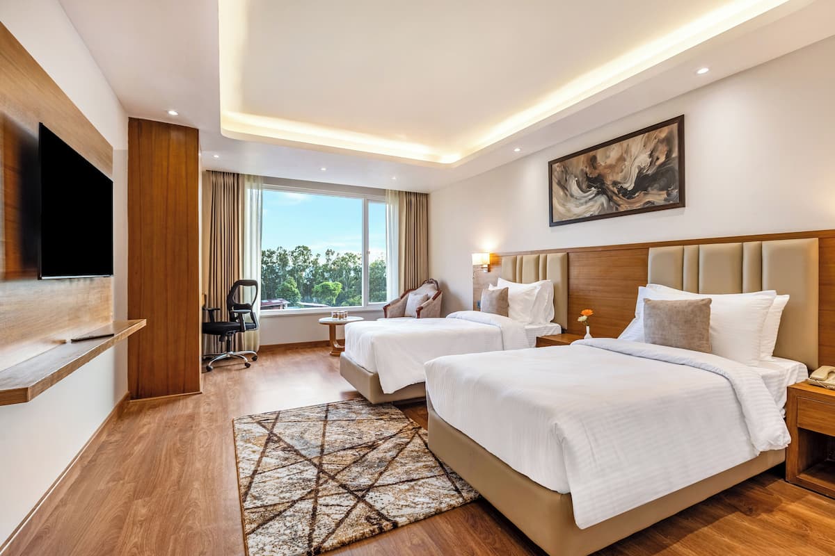 Une chambre d’hôtel avec deux lits, un téléviseur à écran plat, un bureau avec une chaise, une fenêtre avec des rideaux et un tableau au mur.