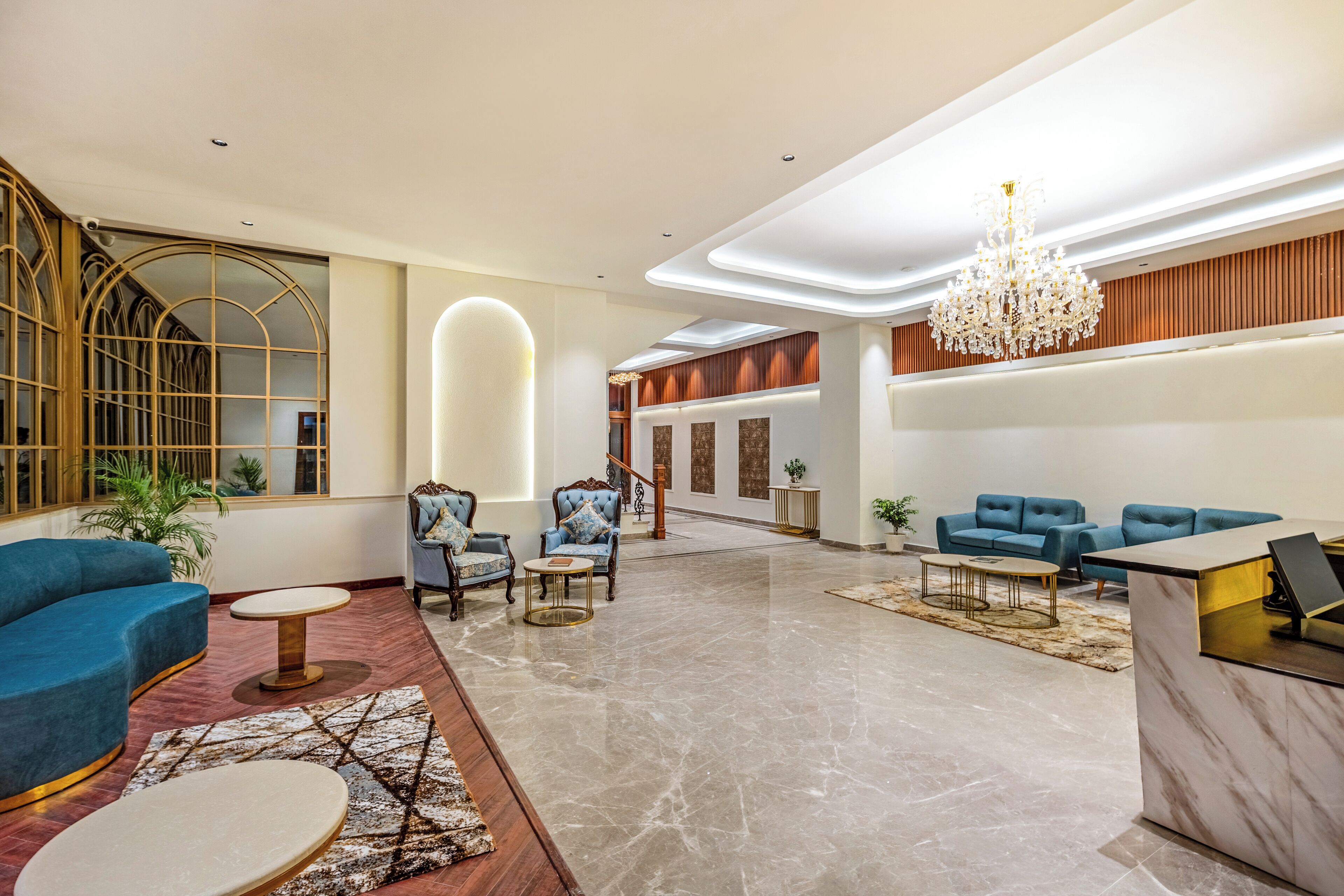 A spacious lobby with a grand chandelier, blue sofas, and a marble floor.