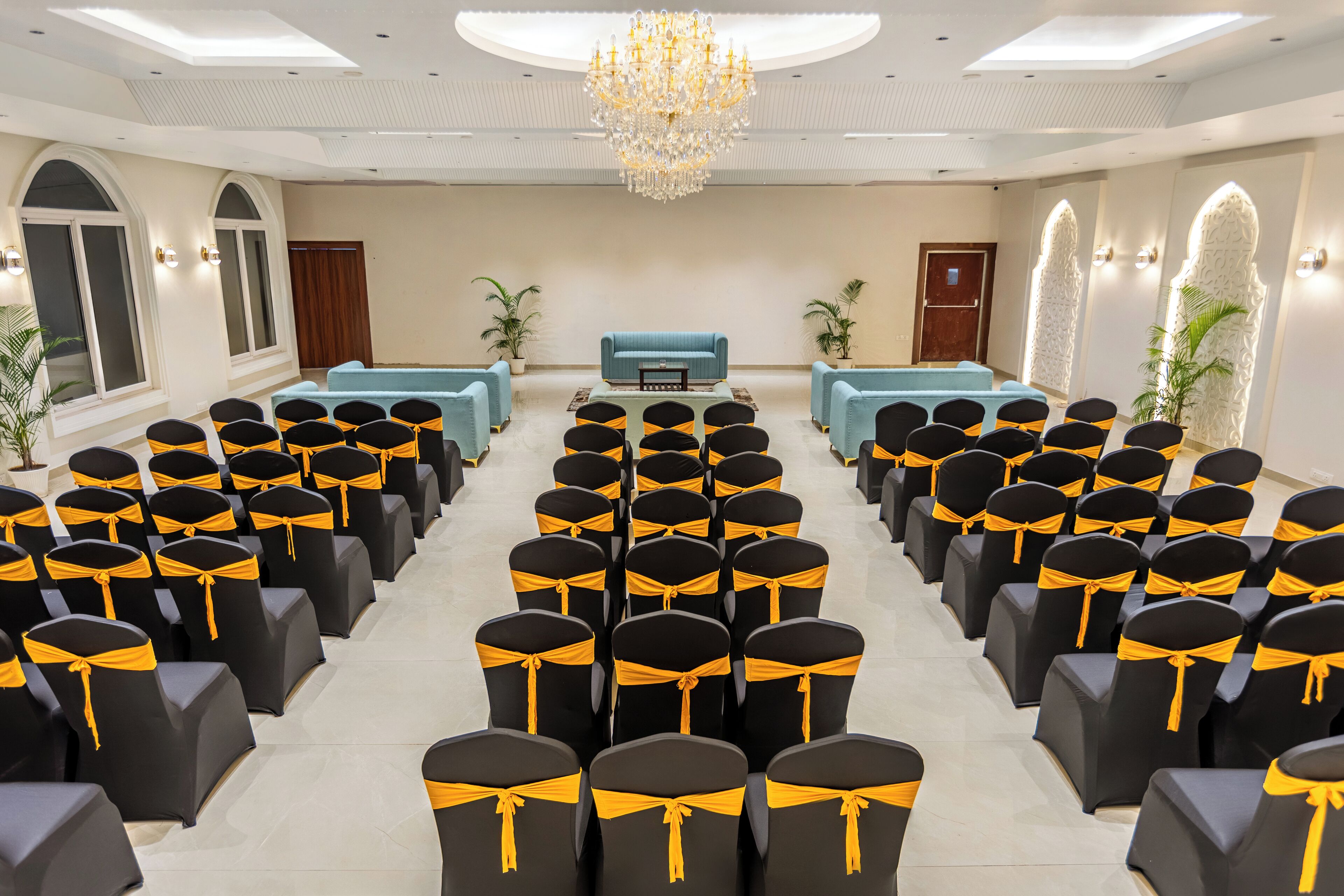 A conference room with rows of black chairs with yellow sashes, a blue sofa, and a chandelier.
