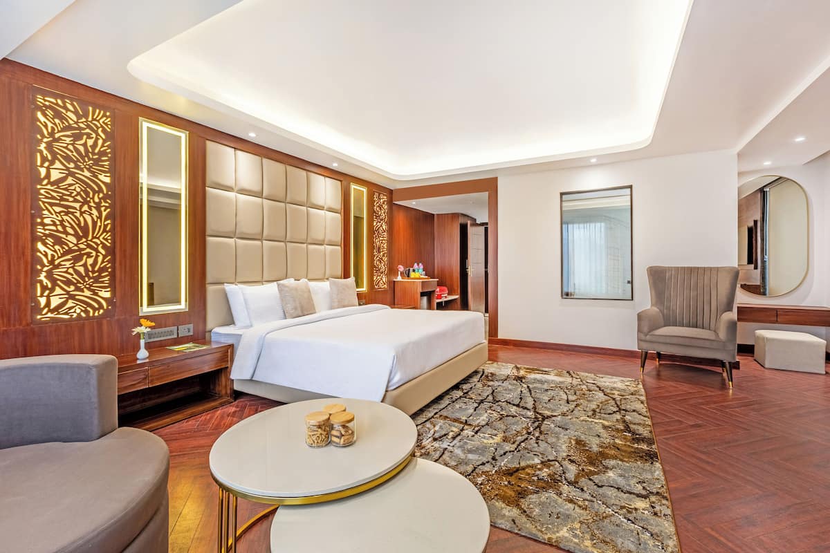 Une chambre d’hôtel moderne avec un grand lit, une table basse ronde, un coin salon et un grand miroir.
