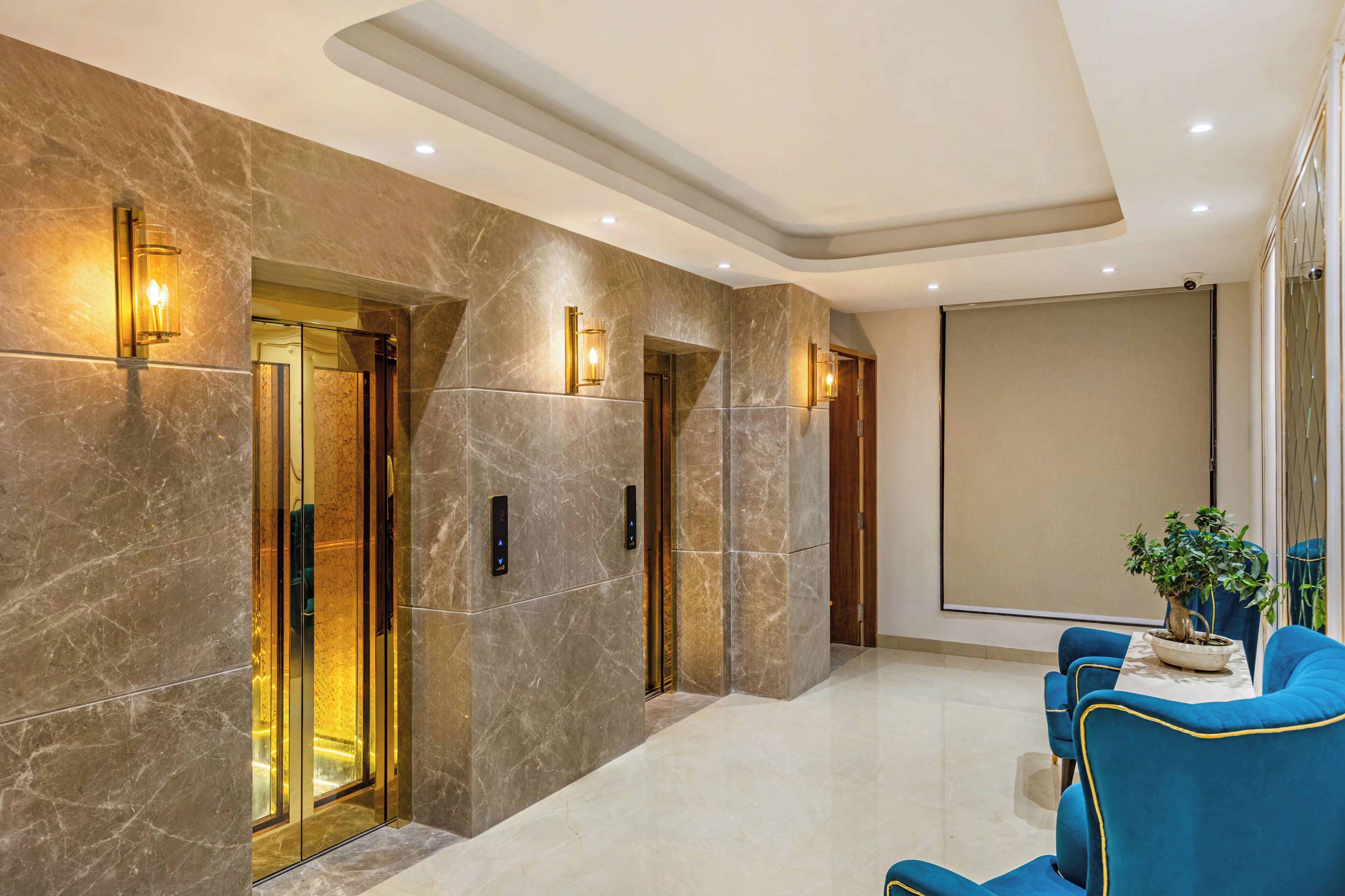 A modern lobby with marble walls, elevator doors, and a seating area with blue chairs.