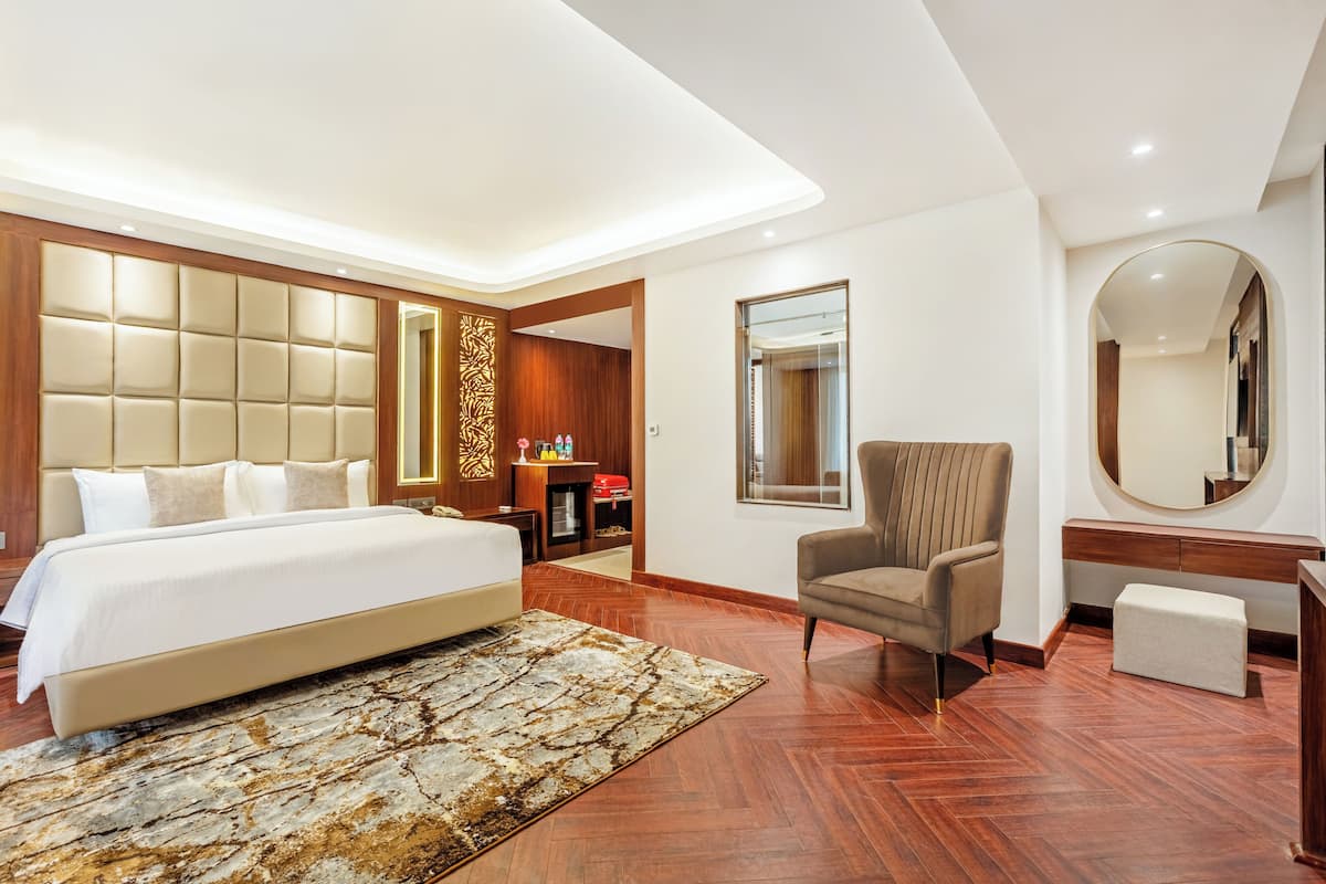 Une chambre d’hôtel moderne dotée d’un grand lit, d’un coin salon avec un fauteuil et un bureau, d’un grand miroir et d’un mur décoratif en bois.