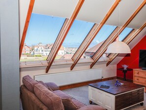 A room with a sloped ceiling, a sofa, a small table, and a radiator. - Atelier (Bridlington)