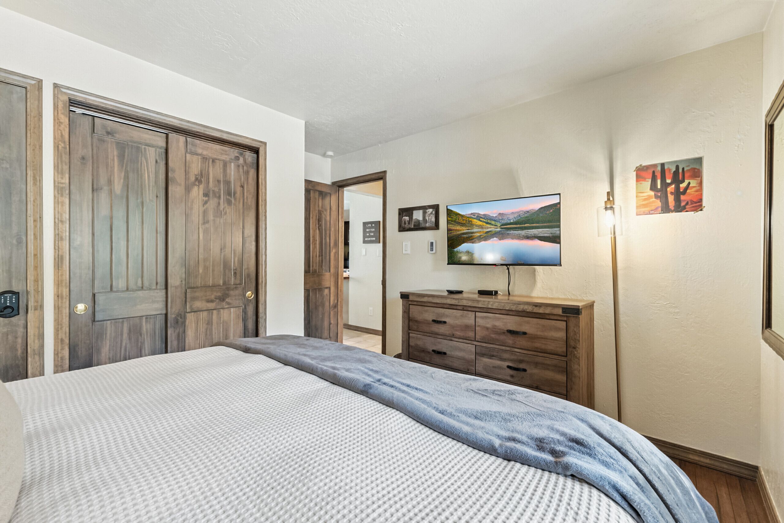 A bedroom with a bed, wooden wardrobe, a television, and a painting on the wall.