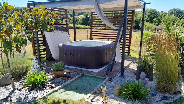 Un jacuzzi bajo una pérgola en un jardín con plantas en macetas y una estatua de Buda.