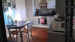 Cocina compacta con armarios blancos, estufa y microondas. Hay una mesa de comedor con sillas y una lámpara.