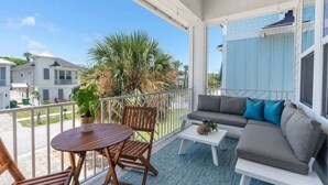 Ein Balkon mit einer Couch, einem Tisch und Stühlen. Im Hintergrund befinden sich ein Blumentopf und eine Palme.