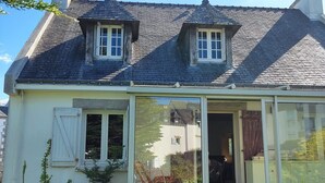 Ein zweistöckiges Haus mit geneigtem Dach, einem Schornstein und einer großen Glasdoor, die zu einer überdachten Veranda führt.