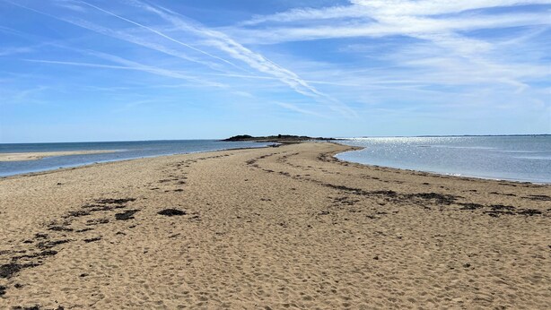 Ein weiter Sandstrand mit sanften Wellen, einem klaren Himmel und einer entfernten Landmasse.